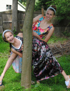 2 girls peaking out from a tree wearing dresses they made