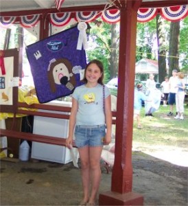 girl standing next to a quilt she made with an award