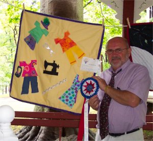 a man standing next to a quilt a kid made with an award