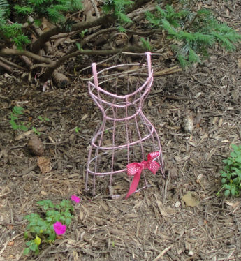 a pink metal dress form in a garden